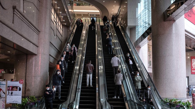 戴着防护口罩的人在2020年2月在香港铜锣湾区由九龙仓控股有限公司经营的时代广场购物中心乘坐自动扶梯。Getty Images。